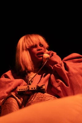 Bathed in red stage lighting, Erykah Badu sings into a vintage telephone receiver on Sept. 22, 2026, at the Everwise Amphitheater at White River State Park, in Indianapolis, Indiana. (Photo/Mia Moore)
