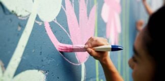 Woman, hand or painting on wall art for mural, creativity or community service at building. Artist, paintbrush or outdoor with color for floral decor, creative process or flowers for aesthetic design