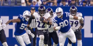 Baltimore Ravens running back Derrick Henry (#22) bursts through the line as Indianapolis Colts defenders, including Jaylon Carlies (#57) and Grover Stewart (#90), pursue him on Sept. 13, 2026, at Lucas Oil Stadium, in downtown Indianapolis, Indiana. (Photo/Walt Thomas)